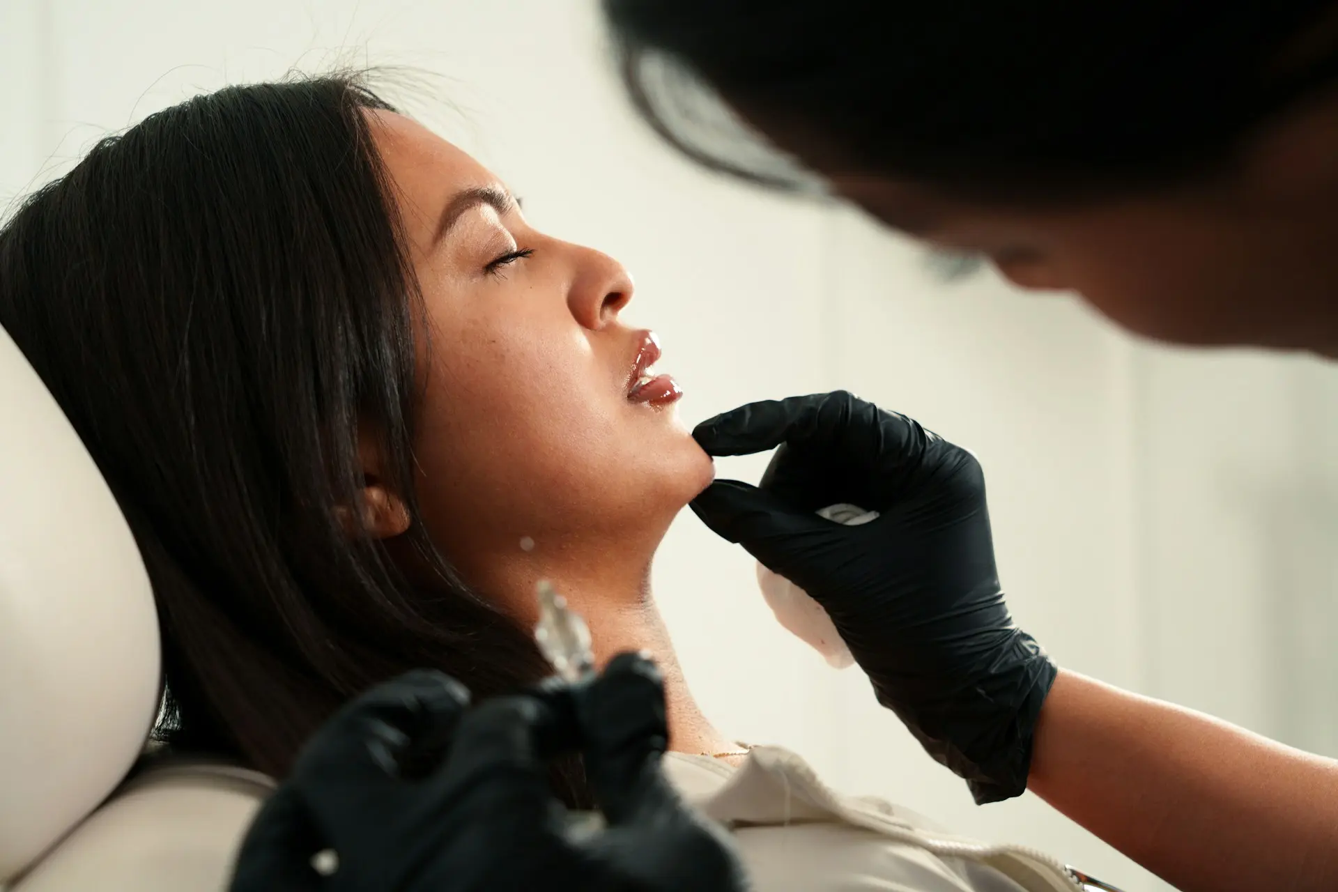 A woman wearing black gloves checking a woman's chin